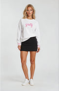 Woman wearing a white sweatshirt with 'golf' printed on it, black skirt, and white sneakers against a white background