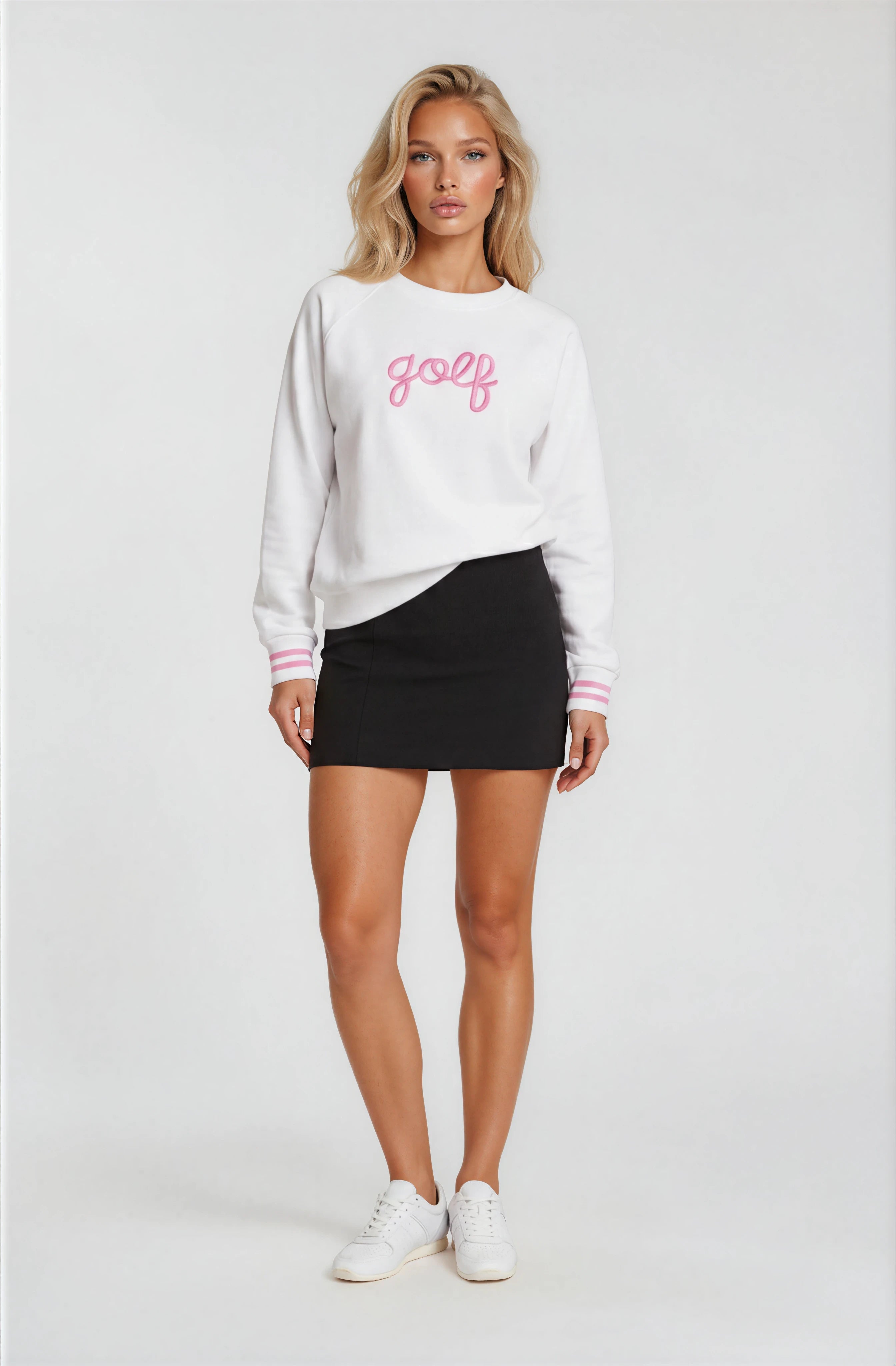 Woman wearing a white sweatshirt with 'golf' printed on it, black skirt, and white sneakers against a white background