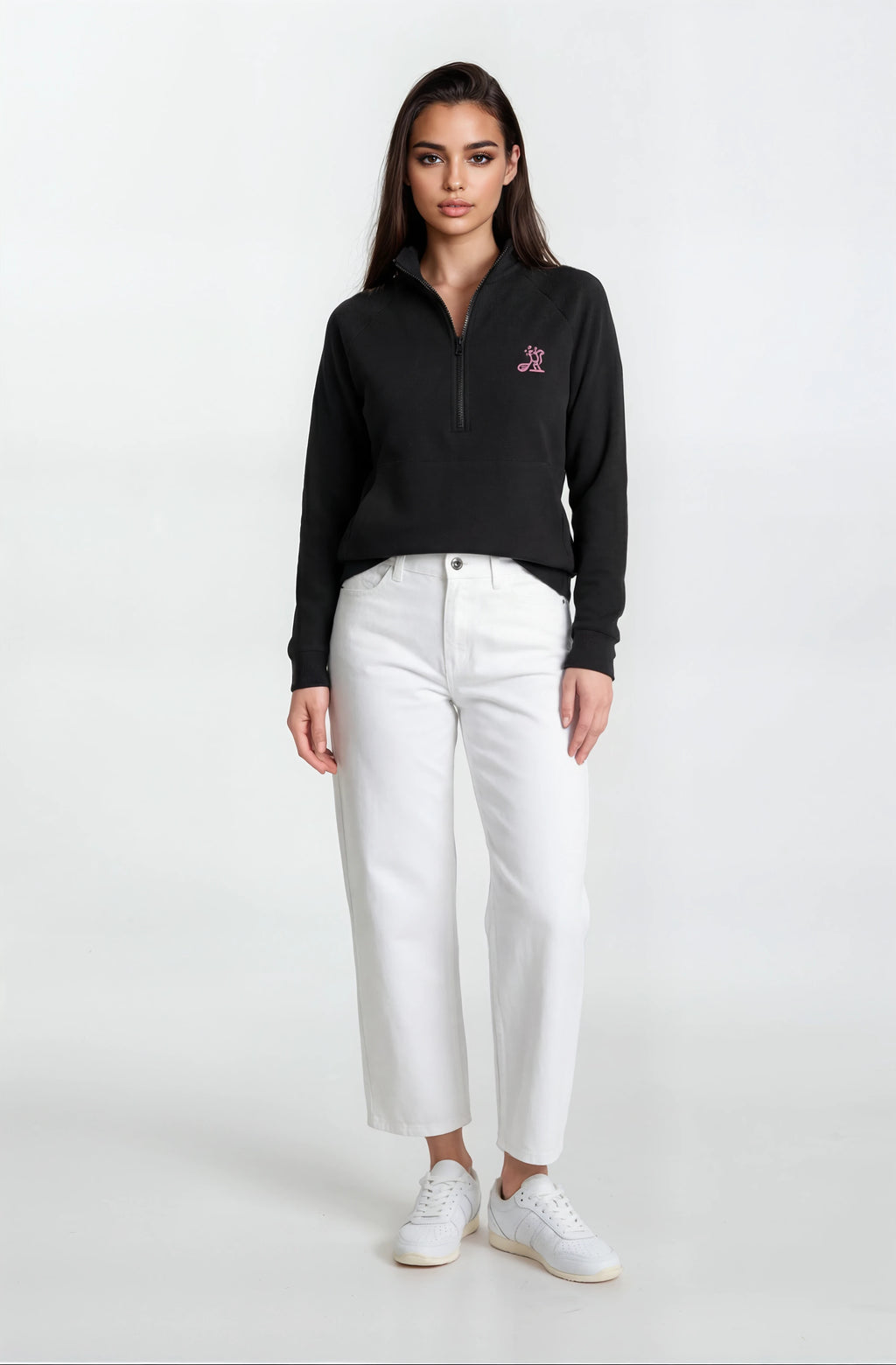 Woman wearing a black sweater with a logo and white pants on a white background