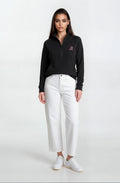Woman wearing a black sweater with a logo and white pants on a white background